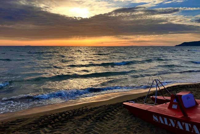 Spiaggia al tramonto con un moscone di salvataggio rosso e mare mosso.
