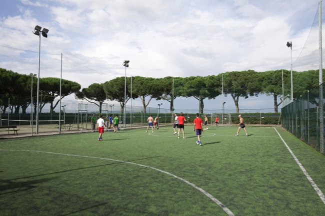 Campo da calcetto all'aperto con persone che giocano sotto un cielo nuvoloso.