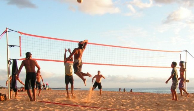Persone giocano a pallavolo sulla spiaggia al tramonto.