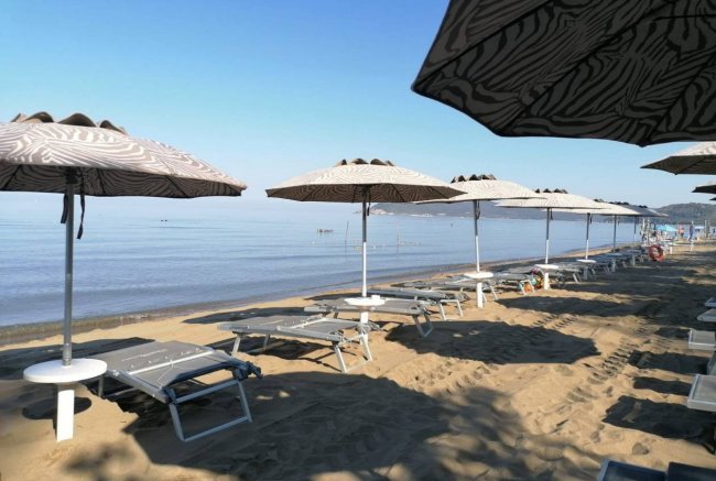 Spiaggia con sdraio e ombrelloni, mare calmo all'orizzonte.