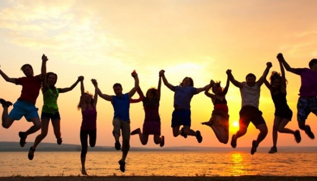 Persone saltano sulla spiaggia al tramonto, tenendosi per mano.