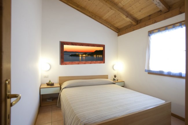 Camera da letto con letto matrimoniale, parete bianca e quadro con paesaggio al tramonto.