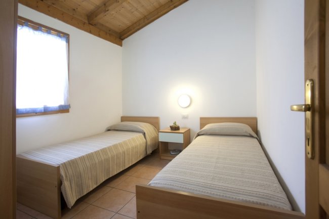 Camera con due letti singoli, pareti bianche e soffitto con travi in legno.