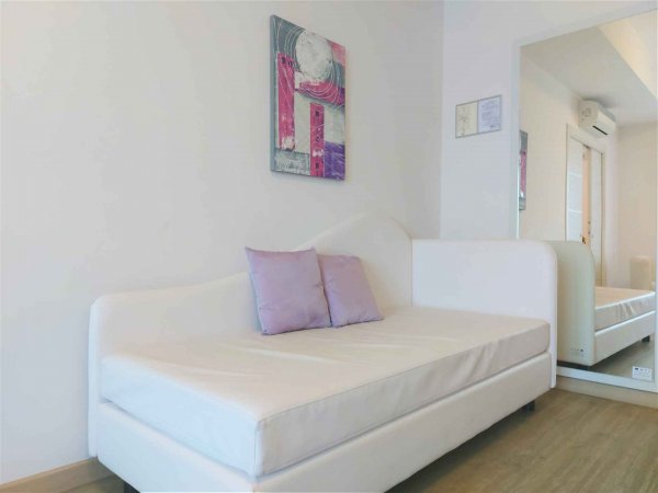 Divano bianco con cuscini viola in una stanza luminosa.