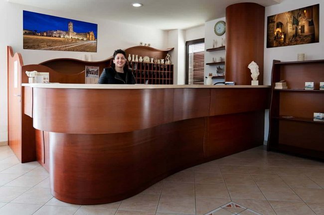 Reception in legno scuro con una persona sorridente dietro al banco.
