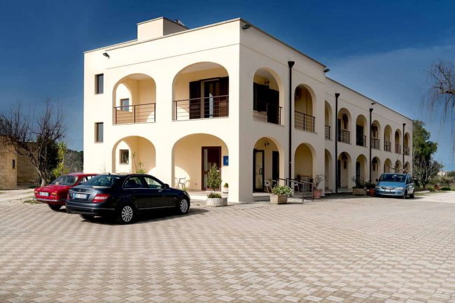 Edificio con archi e balconi, auto parcheggiate davanti.