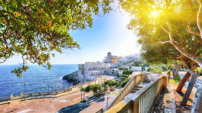 Panorama costiero con edifici storici, mare e alberi al tramonto.