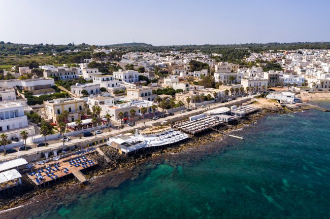 Veduta aerea di una città costiera con edifici bianchi e un mare turchese.