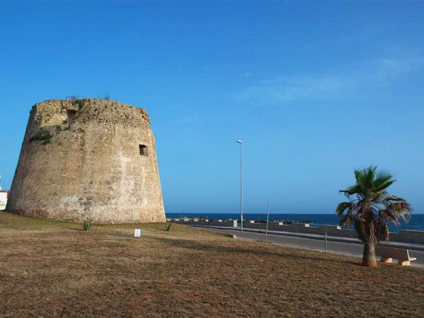 Torre in pietra vicino al mare su un prato arido, con un cielo blu sullo sfondo.