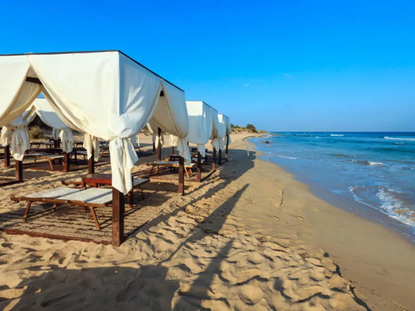 Spiaggia sabbiosa con gazebo bianchi e lettini sotto un cielo limpido.