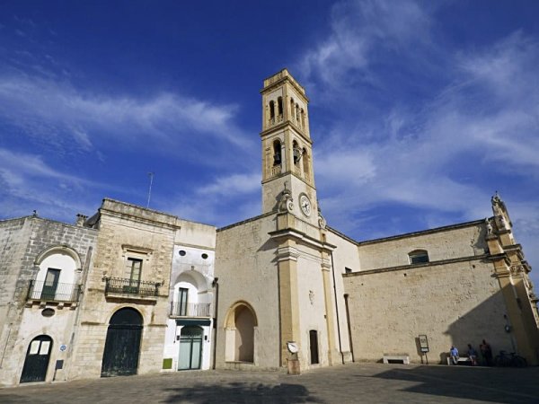 Chiesa storica con torre campanaria sotto un cielo blu e nuvole.