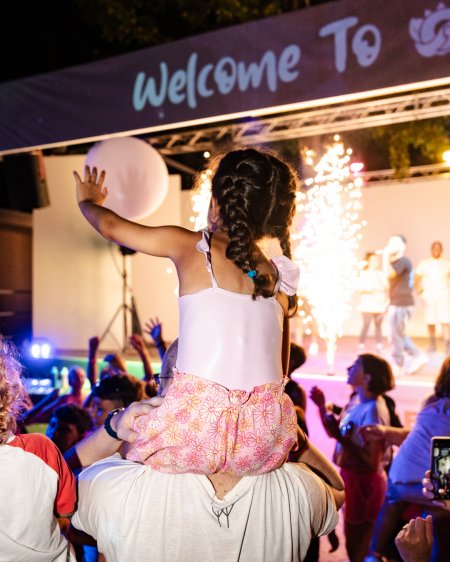 Bambina sulle spalle di un adulto a un evento festivo.
