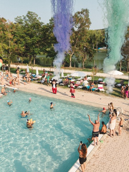 Piscina all'aperto con persone e fumo colorato.