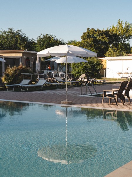 Piscina con sdraio e ombrelloni bianchi.