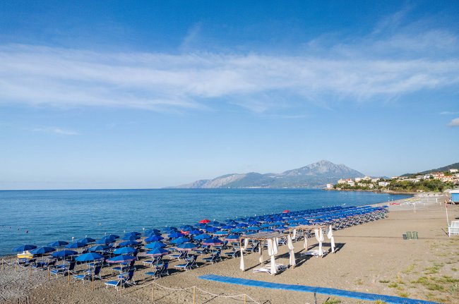 Spiaggia con ombrelloni blu e mare calmo.
