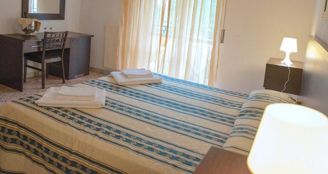 Camera con letto matrimoniale, copriletto a righe blu, scrivania e lampada accesa.