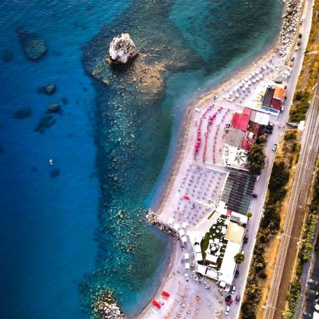 Vista aerea di una spiaggia con ombrelloni e mare azzurro, stradina costiera.