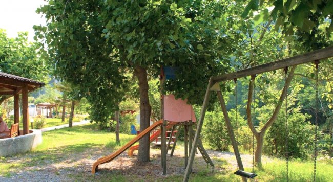 Parco giochi all'aperto con uno scivolo arancione sotto un albero e un'altalena accanto.