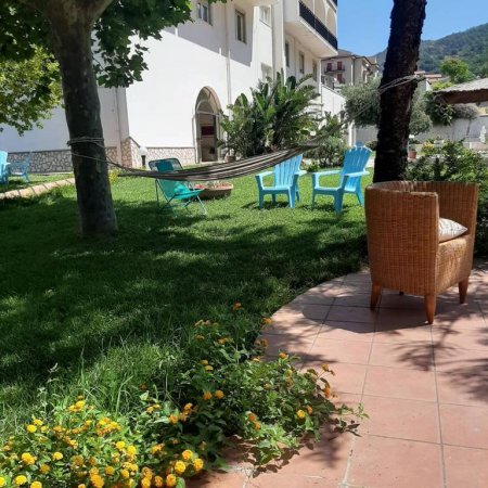 Un giardino con sedie azzurre, una poltrona di vimini, amache e fiori gialli.