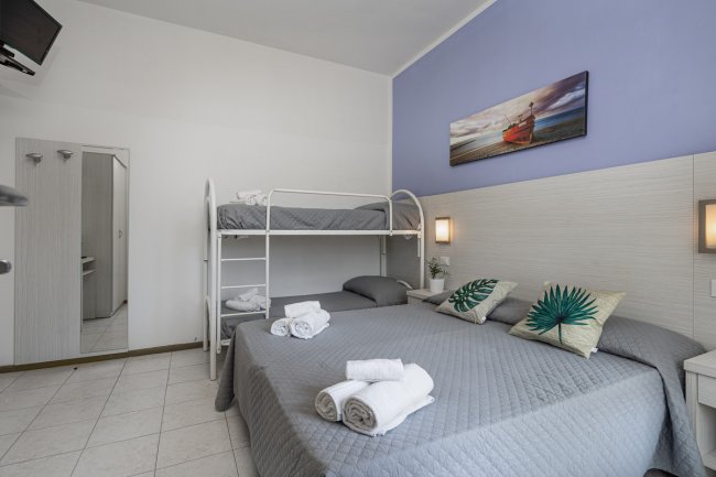 Camera con letto matrimoniale, letto a castello, lenzuola grigie e quadro sopra il letto.