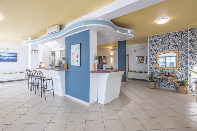 Una reception moderna con bancone curvo, sedie alte e pareti decorate con piante e dipinti.