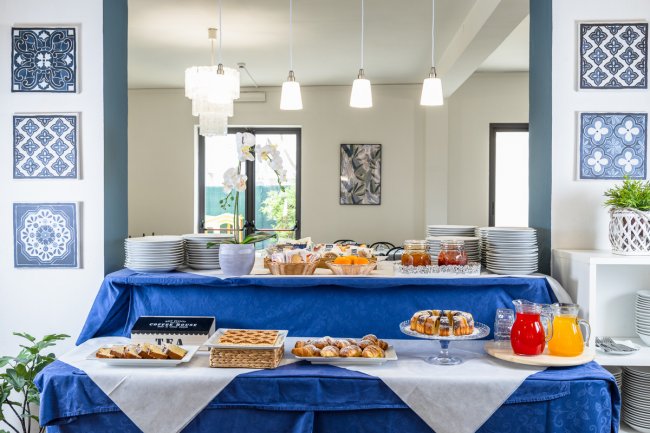 Buffet per la colazione con torte, succhi e cibi vari. Decorazioni alle pareti e lampade sospese.