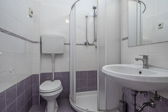 Un piccolo bagno con doccia angolare, lavandino e WC con piastrelle viola e bianche.