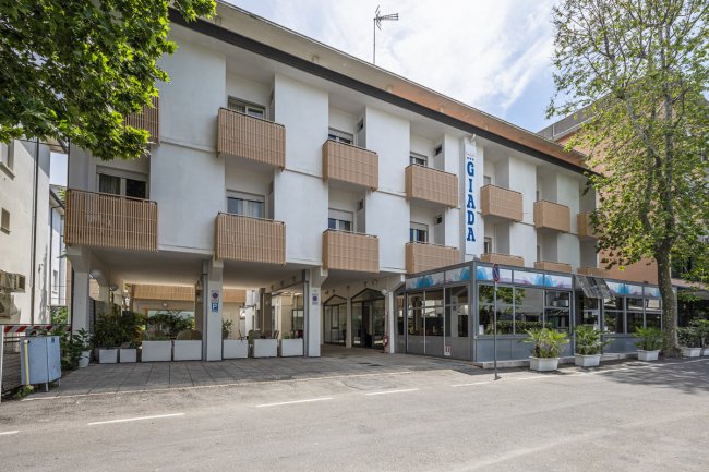 L'esterno di un edificio con balconi quadrati e una veranda vetrata, con piante all'ingresso.