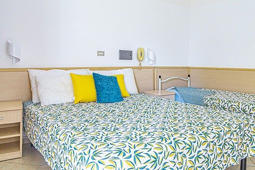 Camera con letto matrimoniale e letti singoli, copriletto floreale e cuscini colorati.