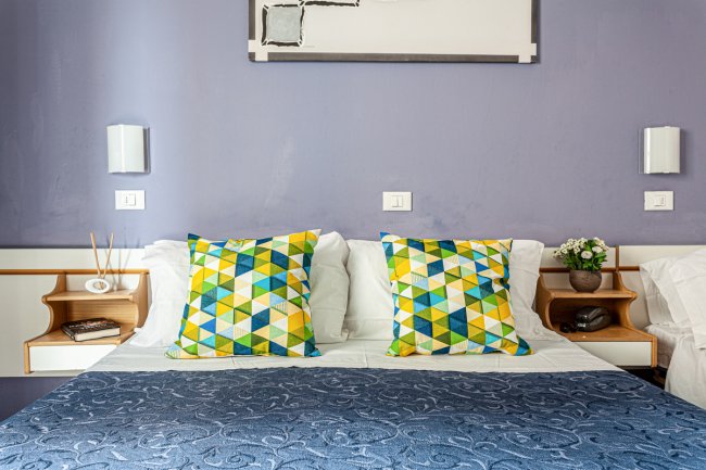Letto con cuscini geometrici colorati in una stanza con pareti viola.