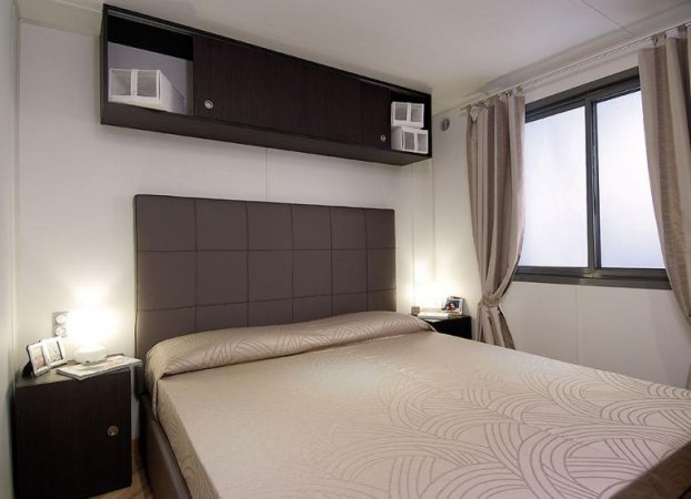 Camera da letto con letto matrimoniale, testiera imbottita e armadietti scuri.