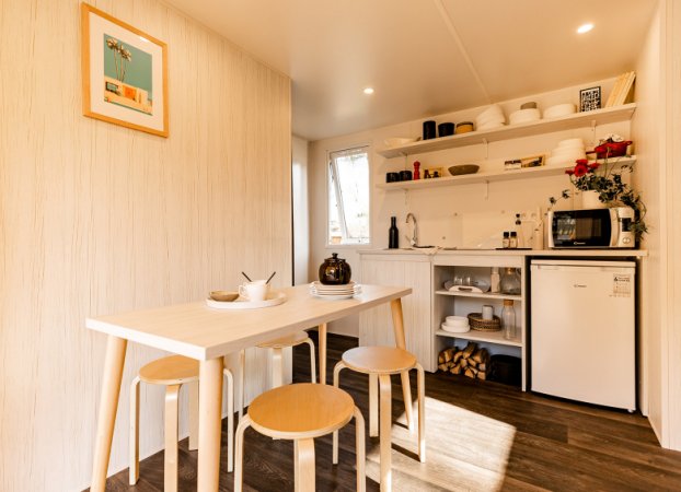 Cucina compatta con tavolo, sgabelli e scaffali aperti.