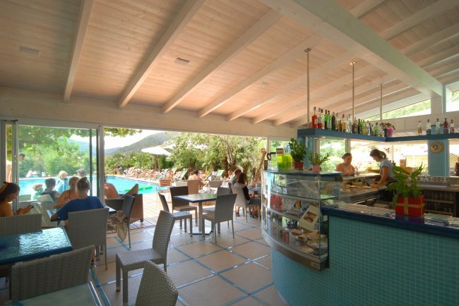 Interno di un bar con vista sulla piscina esterna, tavoli e sedie moderne.