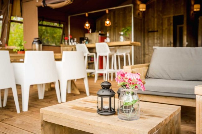Area relax con tavolino in legno, lanterna e vasetto con fiori rosa, arredamento moderno.