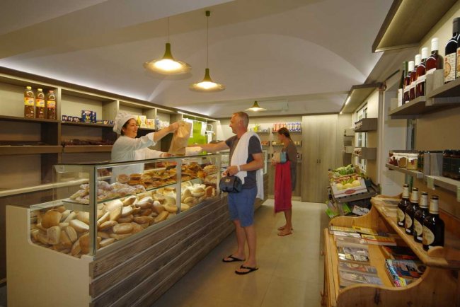 Interno di un negozio di alimentari con pani assortiti e persone che fanno acquisti.