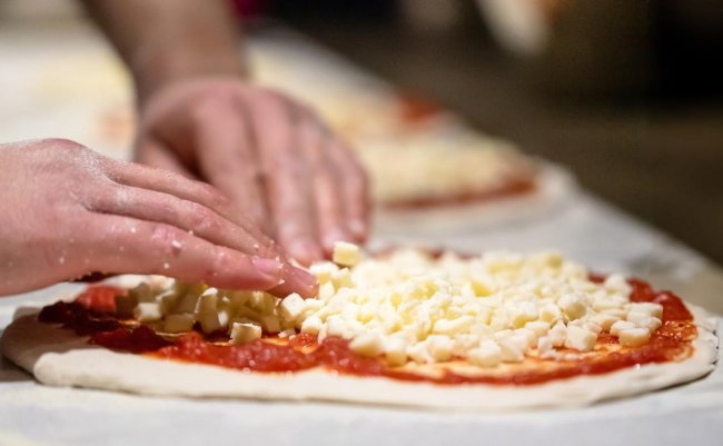 Mani che aggiungono cubetti di formaggio su una pizza con salsa di pomodoro.