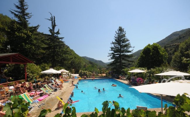 Piscina all'aperto con persone che nuotano, circondata da lettini e ombrelloni.