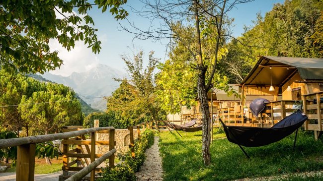 Un campeggio con tende, alberi e amache, circondato da montagne e verde.