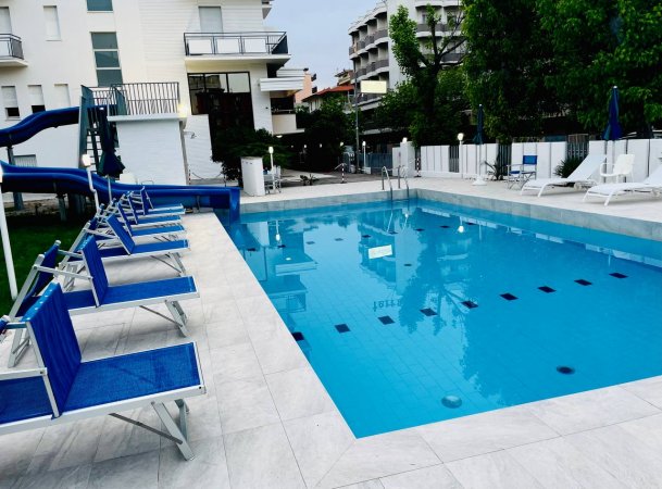 Piscina con sedie a sdraio blu e scivolo.