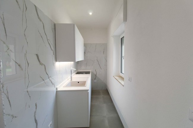 Cucina stretta con mobili bianchi e pareti marmoree.