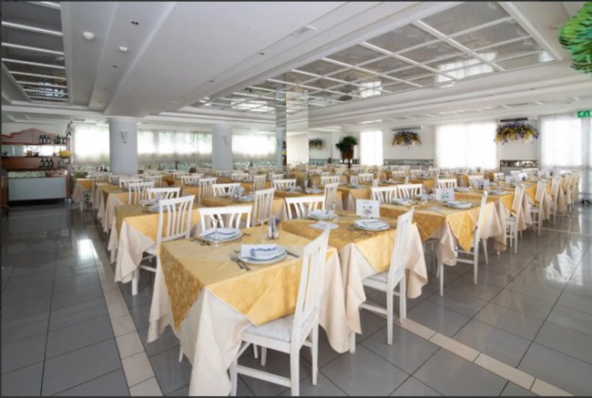 Sala da pranzo con tavoli apparecchiati e sedie bianche.