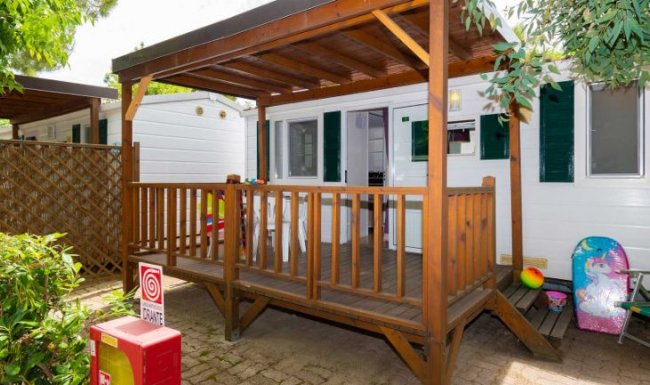 Veranda in legno con staccionata, accanto a roulotte bianca.