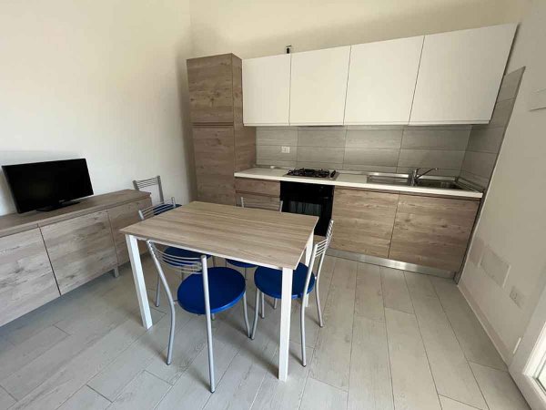 Cucina moderna con tavolo, sedie blu e mobili in legno chiaro.