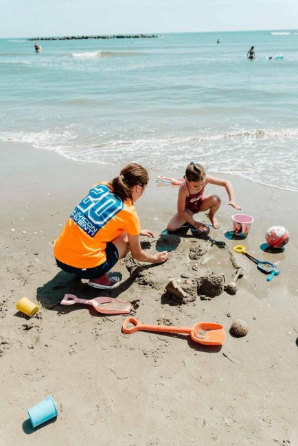 Due persone giocano sulla spiaggia con palette e secchielli.