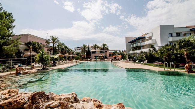 Piscina all'aperto circondata da edifici e palme.