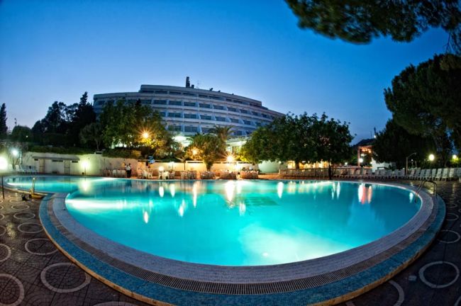Piscina illuminata di sera con edificio sullo sfondo.