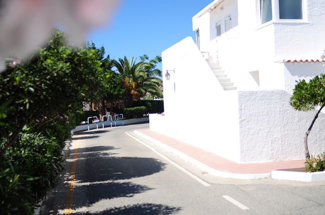 Strada curvilinea con edificio bianco e vegetazione.