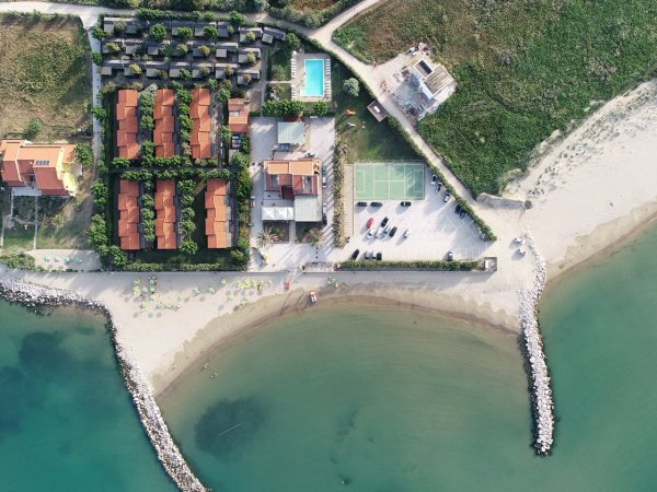 Vista aerea di un complesso con piscina, villette e spiaggia.