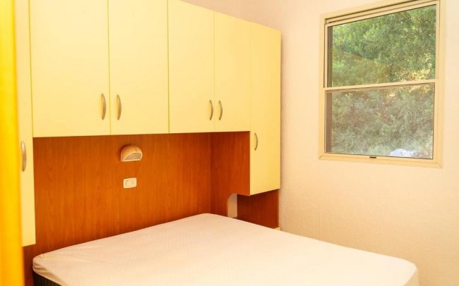 Camera da letto con armadi gialli sopra un letto matrimoniale, finestra con vista sul verde.