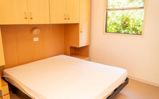Camera da letto con armadi in legno chiaro, letto matrimoniale e finestra.